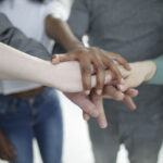 Canva - Crop diverse colleagues stacking hands together during training in office