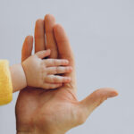 Canva - Crop person touch palms with newborn baby on gray backdrop